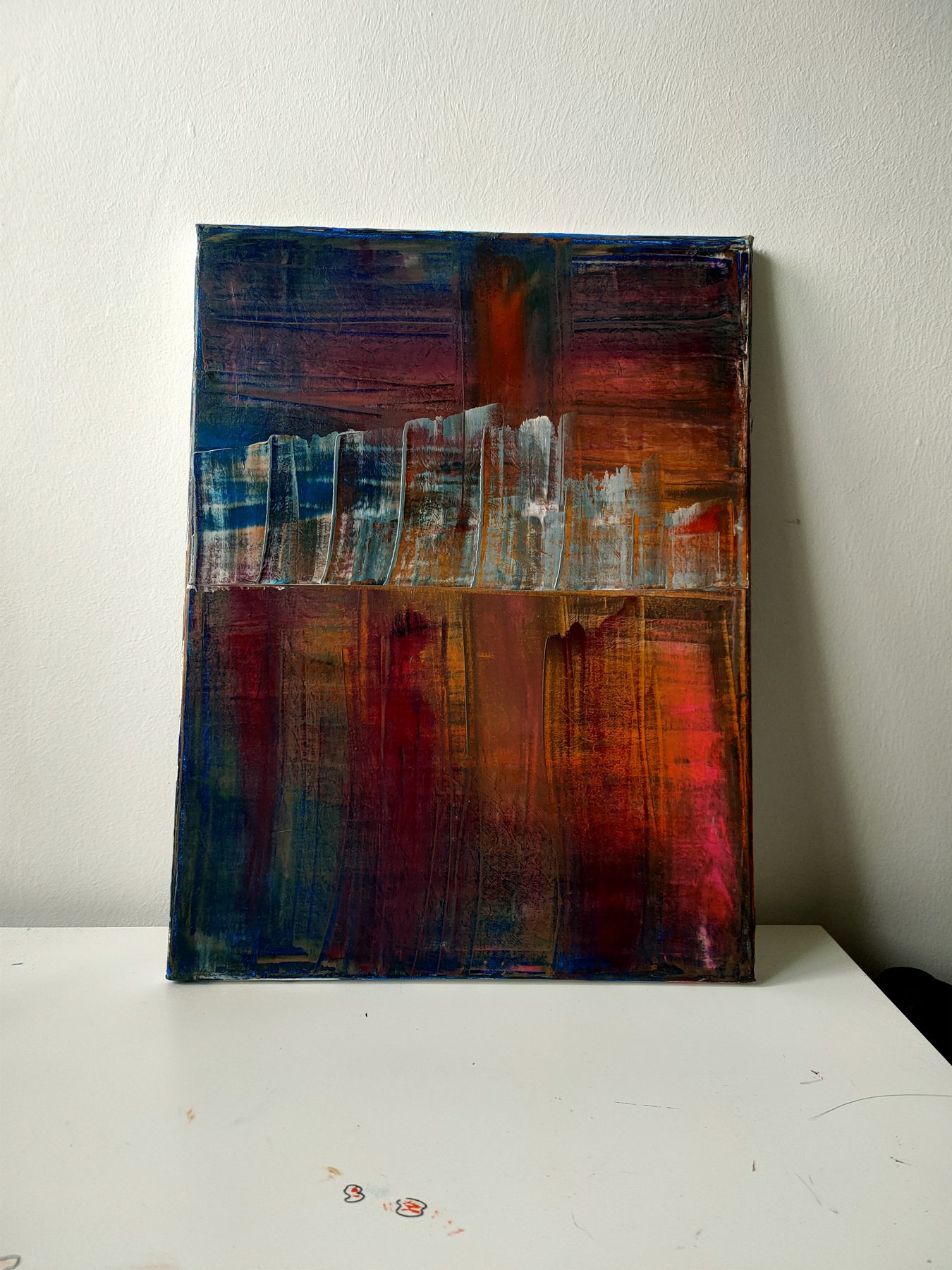 Deep reds, blues and umber worked in crossing vertical and horizontal strokes, with a pale scraped band across the middle.