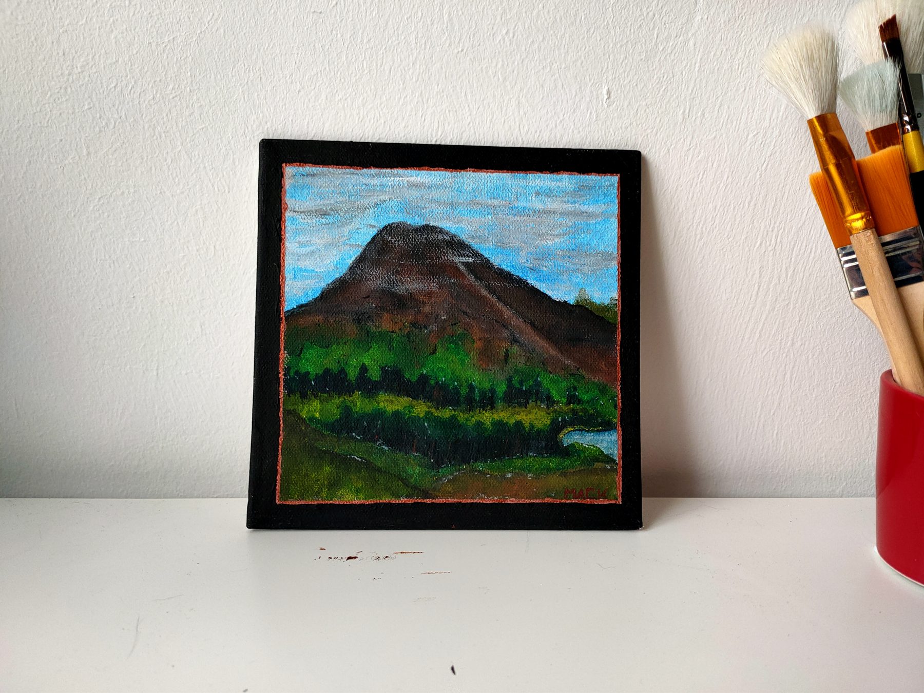 A brown mountain above green foothills under a pale sky, in a black frame.