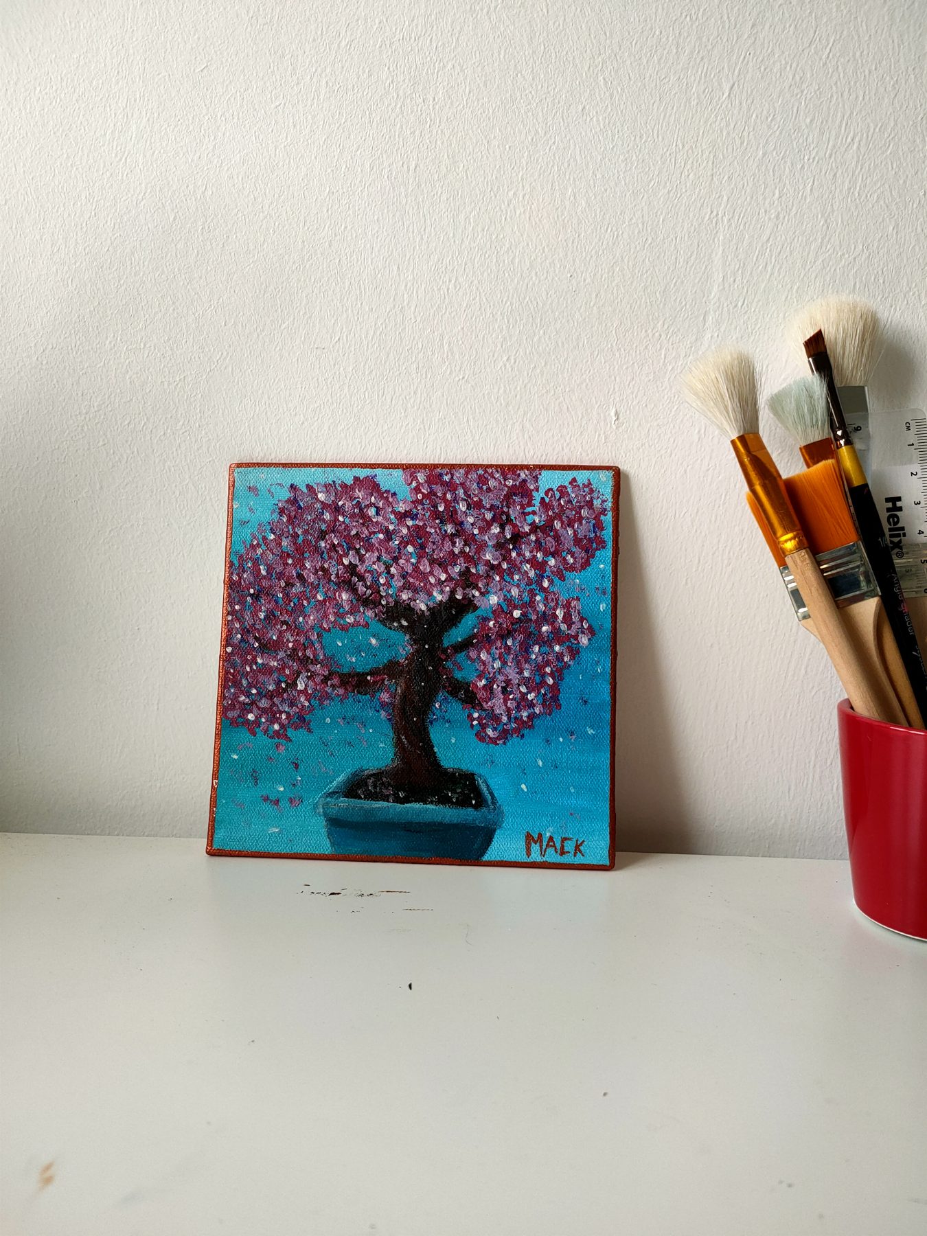 A cherry blossom bonsai in a pot against a teal ground.